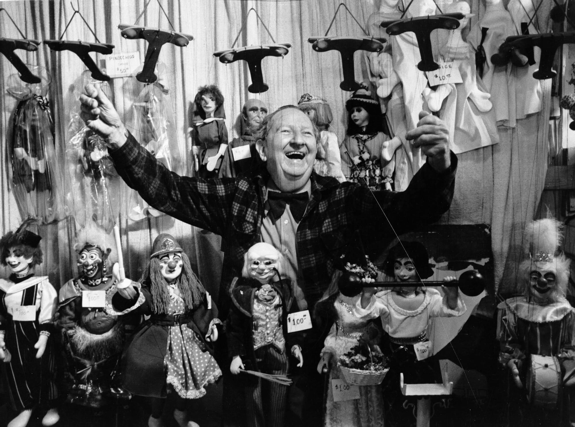 A Smiling Harry Burnett poses with arms extended surrounded by Puppets